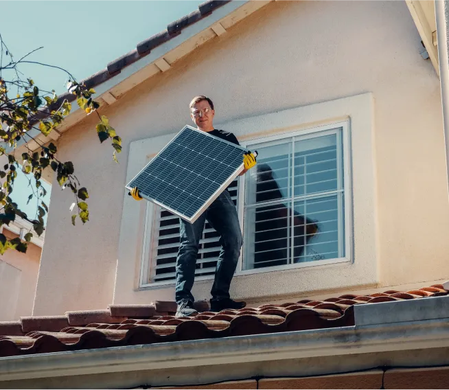 A Person carrying a Solar Panal while standing on a roof